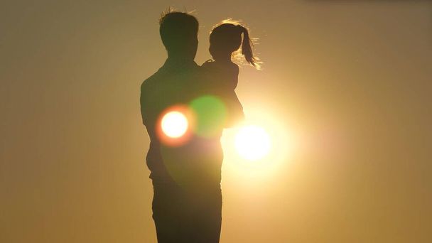 日没の娘とお父さんの日のシルエット。娘は両腕を組んで父の腕の中に飛び立つ。その少女は最愛の親の腕の中で空に浮かぶ。分離 - 写真・画像