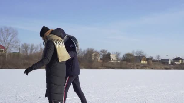 Ο νεαρός μαθαίνει στην κοπέλα του να κάνει πατινάζ σε παγωμένη λίμνη στο δάσος. - Πλάνα, βίντεο