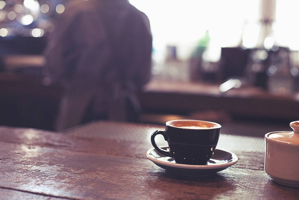 ζεστό φλιτζάνι καφέ στο πάγκο καφετέρια με σερβιτόρα γυναίκα στο παρασκήνιο. - Φωτογραφία, εικόνα