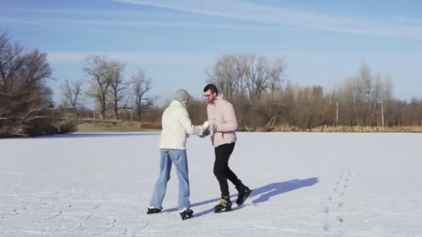 Giovane uomo insegna alla sua ragazza a cavalcare pattinaggio su ghiaccio all'indietro sul lago ghiacciato nella foresta - Filmati, video