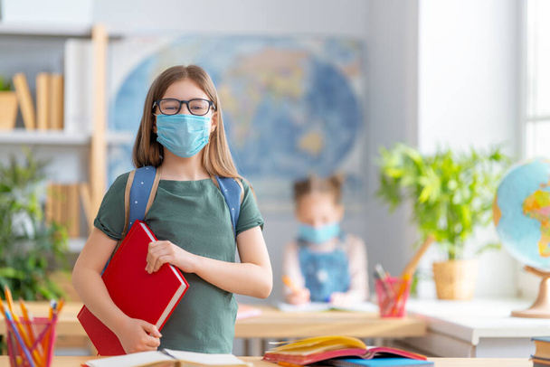 Back to school! Cute industrious children are sitting at  desks indoors. Kids are wearing facemasks learning in class. - Foto, Imagem