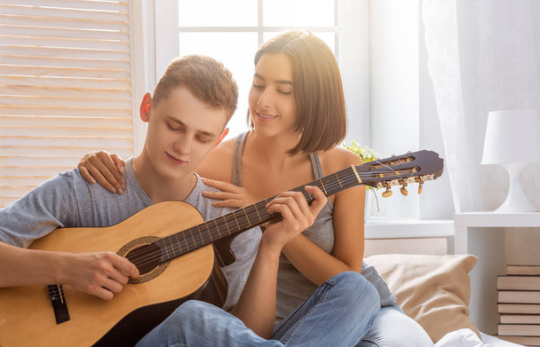 Happy couple in love. Stunning sensual portrait of young stylish fashion couple indoors. Young man playing guitar for his beloved girl. - Foto, Imagem