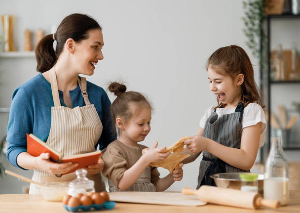 Happy loving family are preparing bakery together. Mother and children daughters girls are cooking cookies and having fun in the kitchen. Homemade food and little helper.    - Foto, imagen