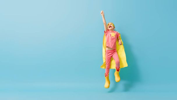 Little child playing superhero. Kid on the background of bright blue wall. Girl power concept. Yellow, pink and  turquoise colors. - Φωτογραφία, εικόνα