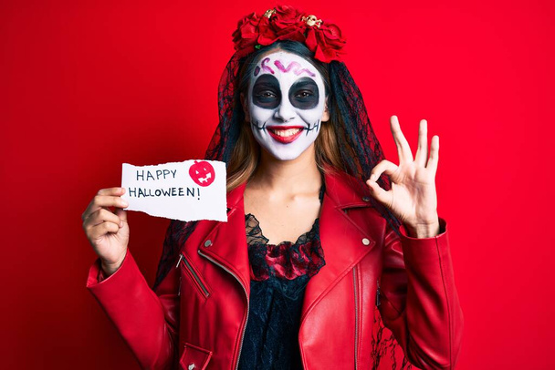 Жінка, одягнена в день мертвих костюмів, тримає щасливий папір на Хеллоуїн робить знак з пальцями, посміхаючись дружній жест відмінний символ
  - Фото, зображення