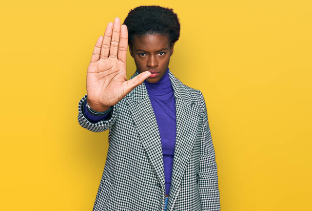 Νεαρή Αφρο-Αμερικανίδα που φοράει καθημερινά ρούχα, σταμάτα να τραγουδάς με την παλάμη του χεριού. προειδοποιητική έκφραση με αρνητική και σοβαρή χειρονομία στο πρόσωπο.  - Φωτογραφία, εικόνα