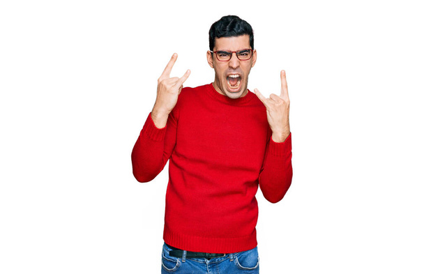 Handsome hispanic man wearing casual clothes and glasses shouting with crazy expression doing rock symbol with hands up. music star. heavy concept.  - Fotografie, Obrázek