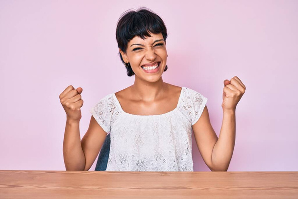Beautiful brunettte woman wearing casual clothes over pink background screaming proud, celebrating victory and success very excited with raised arms  - Photo, Image