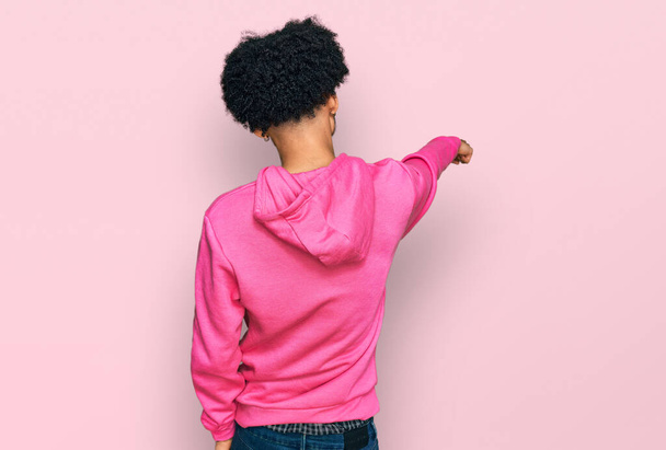 Nuori afrikkalainen amerikkalainen mies afro hiukset yllään rento vaaleanpunainen huppari poseeraa taaksepäin osoittaen sormella eteenpäin  - Valokuva, kuva