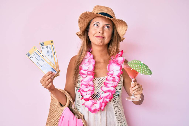 Orta yaşlı İspanyol bir kadın Hawai Lei Lei marka bir kart ve kokteyl tutuyor. Gülümsüyor ve başka tarafa bakıyor..  - Fotoğraf, Görsel