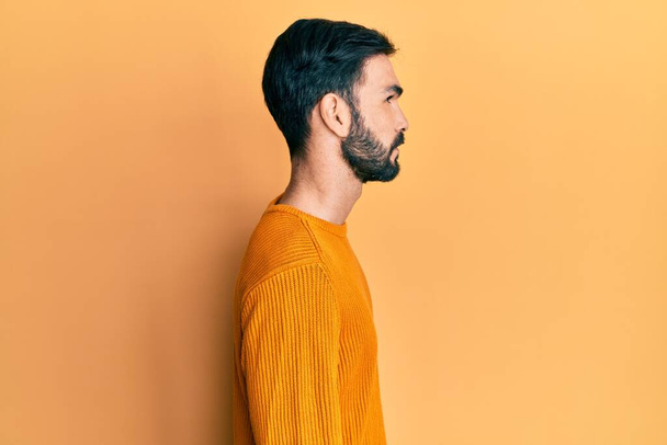 Молодий іспаномовний чоловік в повсякденному одязі, дивлячись на бік, розслабляє профільну позу з природним обличчям з впевненою посмішкою
.  - Фото, зображення