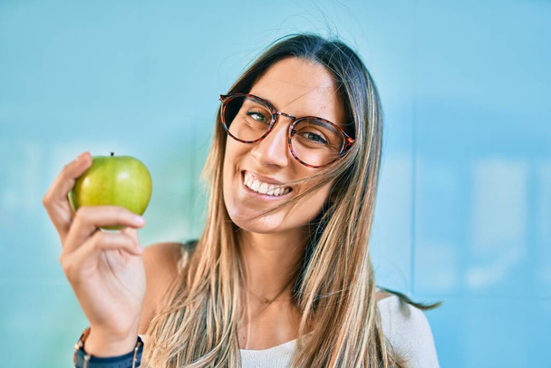 Young caucasian woman smiling happy eating green apple  at the city. - Φωτογραφία, εικόνα