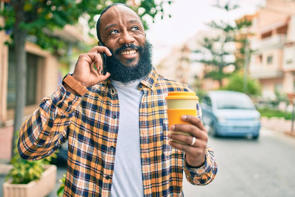 Bello uomo afroamericano moderno con la barba che parla al telefono in città con un sorriso felice - Foto, immagini