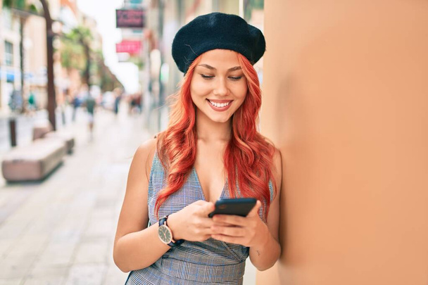 Menina ruiva jovem vestindo estilo francês usando smartphone na cidade. - Foto, Imagem