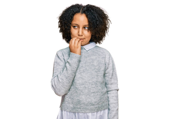 Νεαρό κοριτσάκι με αφρο μαλλιά που φοράει καθημερινά ρούχα που φαίνονται στρεσαρισμένα και νευρικά με τα χέρια στο στόμα να δαγκώνουν νύχια. πρόβλημα άγχους.  - Φωτογραφία, εικόνα