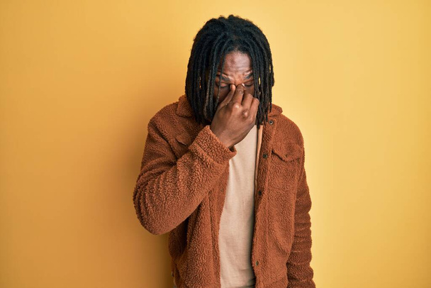 ブラウンのレトロなジャケットを着ているアフリカ系アメリカ人の男性は、鼻と目をこすり疲れや頭痛を感じて疲れている。ストレスとフラストレーションの概念.  - 写真・画像