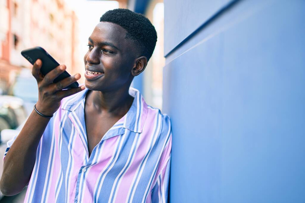 Νεαρός Αφροαμερικάνος χαμογελαστός χαρούμενος μιλώντας στο smartphone στο δρόμο της πόλης. - Φωτογραφία, εικόνα