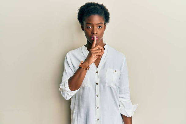 Молода афроамериканська дівчина в повсякденному одязі просить мовчати, натискаючи пальцем на губи. тиша і таємна концепція.  - Фото, зображення