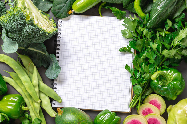 Fresh vegetables and herbs laid out around a notebook for recipes. Top view, place for text. - Photo, image