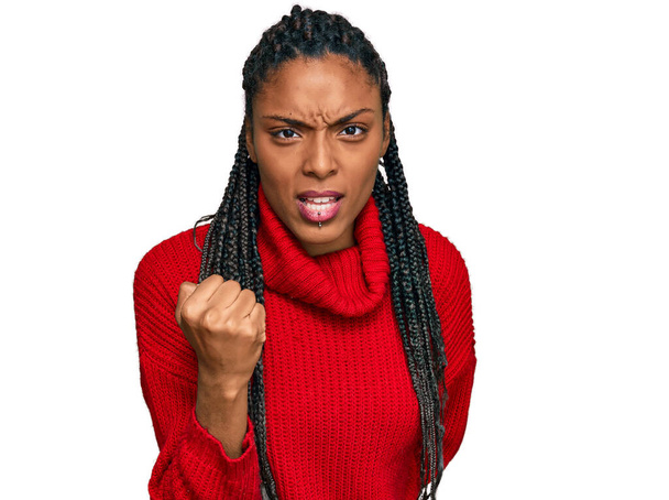 Mujer afroamericana vistiendo suéter casual de invierno enojado y loco levantando el puño frustrado y furioso mientras gritaba con ira. rabia y concepto agresivo.  - Foto, imagen