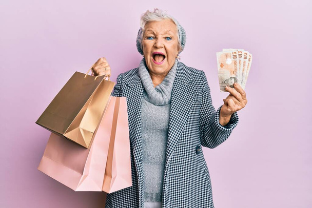 Son sınıf gri saçlı kadın elinde alışveriş poşetleri ve İngiliz banknotları tutarken kahkahalarla gülüyor..  - Fotoğraf, Görsel