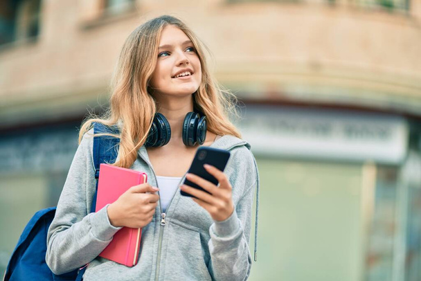 Estudante caucasiano bonito adolescente sorrindo feliz usando smartphone na cidade. - Foto, Imagem