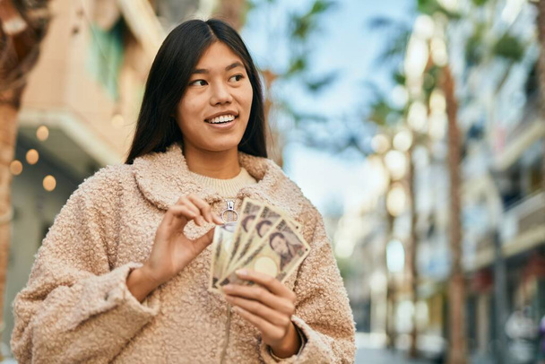 Nuori aasialainen nainen hymyilee onnellinen laskettaessa Japanin jenin seteleitä kaupungissa. - Valokuva, kuva
