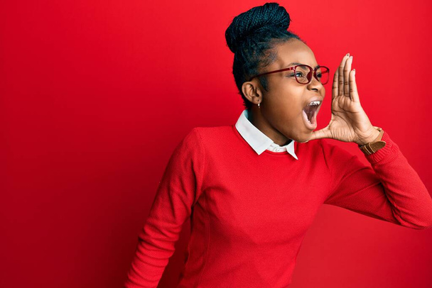 若いアフリカ系アメリカ人の女性は、カジュアルな服や眼鏡を着て大声で叫び、口の上に手で横に叫んでいる。コミュニケーションの概念.  - 写真・画像