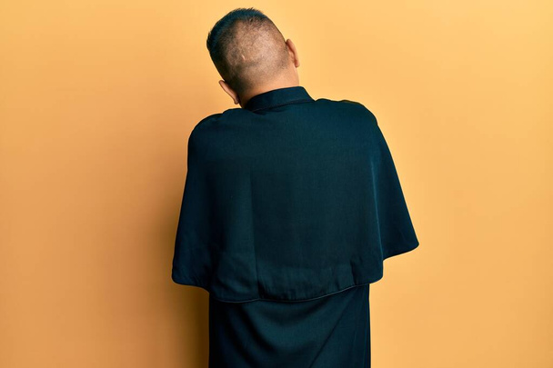 Молодий латинський священик стоїть над жовтим тлом, обіймаючи себе щасливим і позитивним ззаду. самодопомоги і самодопомоги
  - Фото, зображення