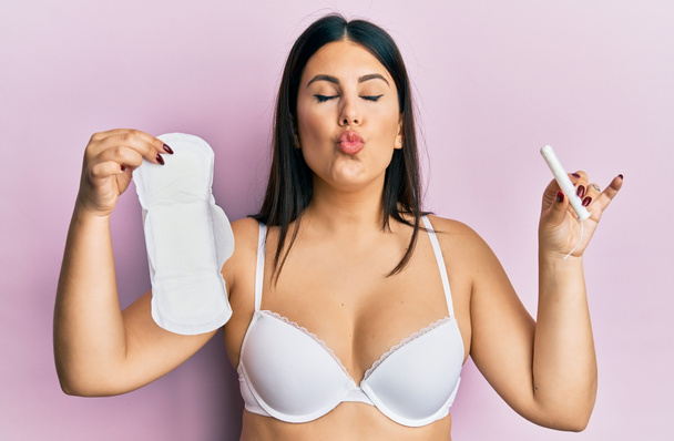 Beautiful brunette woman holding sanitary pad and cotton tampon looking at the camera blowing a kiss being lovely and sexy. love expression.  - Φωτογραφία, εικόνα