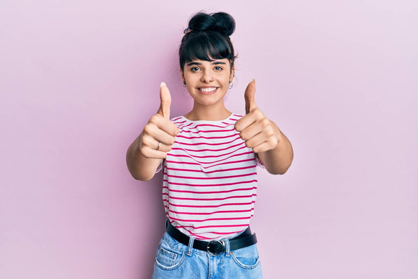 Nuori latino tyttö yllään rento vaatteita hyväksymisestä tekee positiivinen ele käsin, peukalot ylös hymyillen ja onnellinen menestykseen. voittajan ele.  - Valokuva, kuva