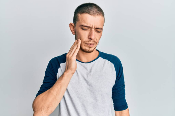 Spaanse jongeman draagt casual kleding aanraken mond met de hand met pijnlijke uitdrukking als gevolg van kiespijn of tandheelkundige ziekte op tanden. tandarts  - Foto, afbeelding