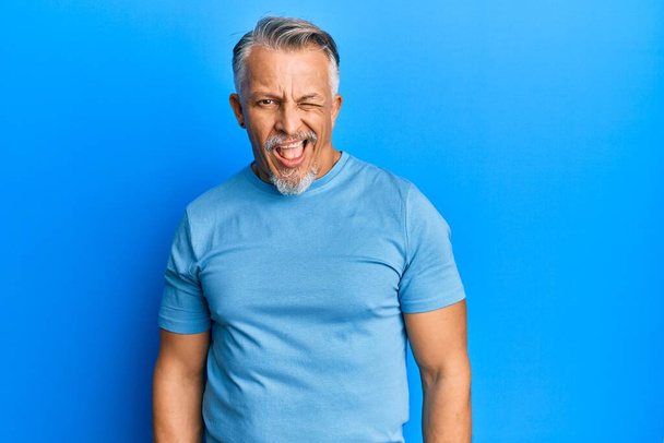 Middelbare leeftijd grijsharige man met casual kleding knipogen naar de camera met sexy uitdrukking, vrolijk en gelukkig gezicht.  - Foto, afbeelding