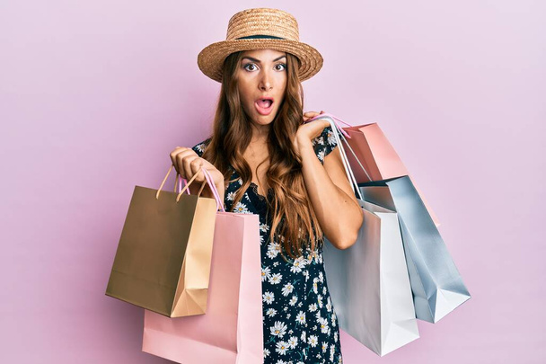 Young brunette woman holding shopping bags afraid and shocked with surprise and amazed expression, fear and excited face.  - Photo, Image