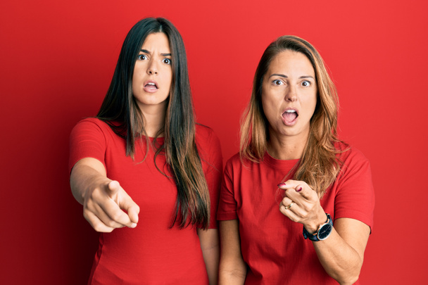 Familia hispana de madre e hija vistiendo ropa casual sobre fondo rojo señalando disgustada y frustrada a la cámara, enojada y furiosa contigo  - Foto, Imagen