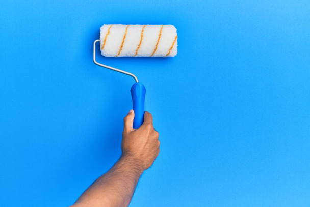 Hand van de Spaanse man schilderen blauwe muur met behulp van verfroller. - Foto, afbeelding