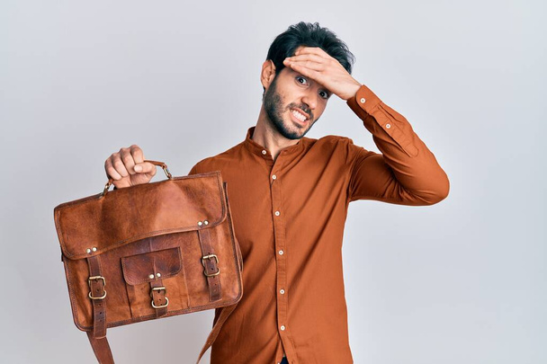 Young hispanic man wearing leather bag stressed and frustrated with hand on head, surprised and angry face  - Zdjęcie, obraz