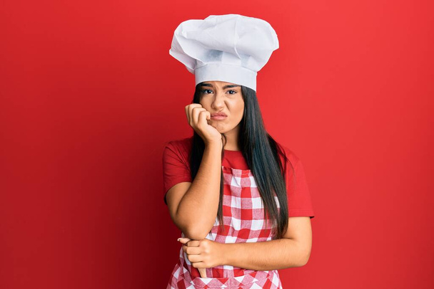 Mladá krásná hispánská dívka nosí pekařskou uniformu a kuchař klobouk myšlení vypadá unaveně a nudí s depresí problémy se zkříženými pažemi.  - Fotografie, Obrázek