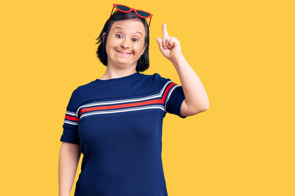 Brunette woman with down syndrome wearing casual clothes pointing finger up with successful idea. exited and happy. number one.  - Foto, Imagen
