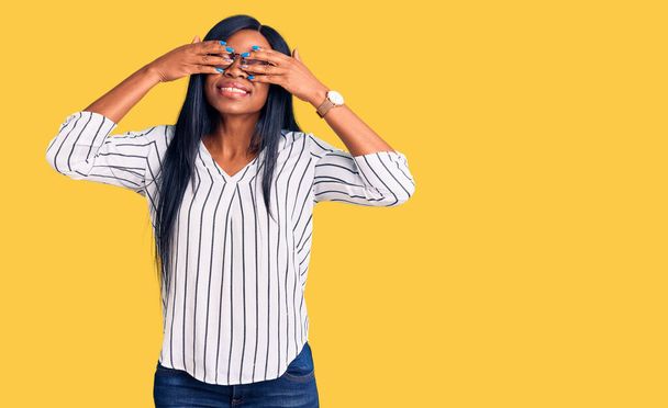 Young african american woman wearing casual clothes and glasses covering eyes with hands smiling cheerful and funny. blind concept.  - Photo, Image
