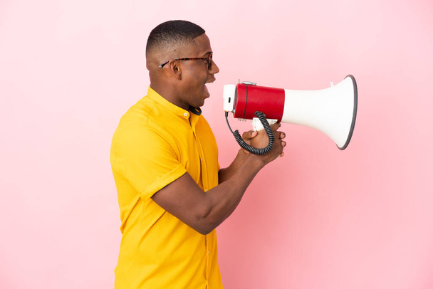 Young latin man isolated on pink background shouting through a megaphone - Foto, Imagem