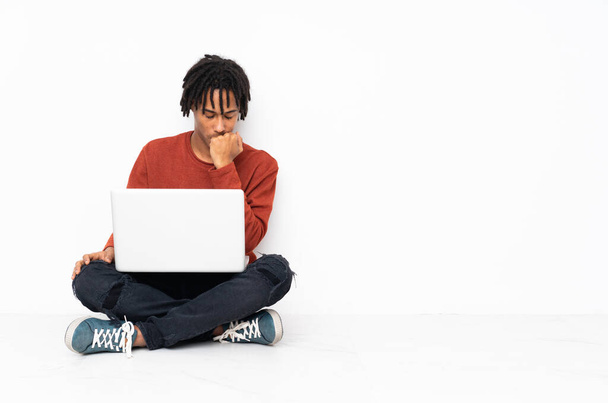 Молодий афроамериканець, що сидить на підлозі і працює зі своїм ноутбуком, сумнівається. - Фото, зображення