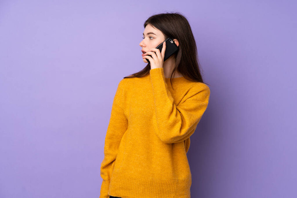 jong Oekraïense tiener meisje over geïsoleerde paarse achtergrond houden van een gesprek met de mobiele telefoon met iemand - Foto, afbeelding