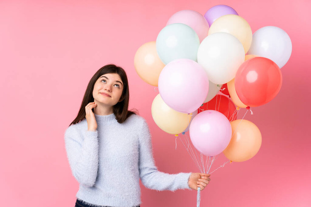 Young Ukrainian teenager girl holding lots of balloons over isolated pink background thinking an idea - Photo, Image