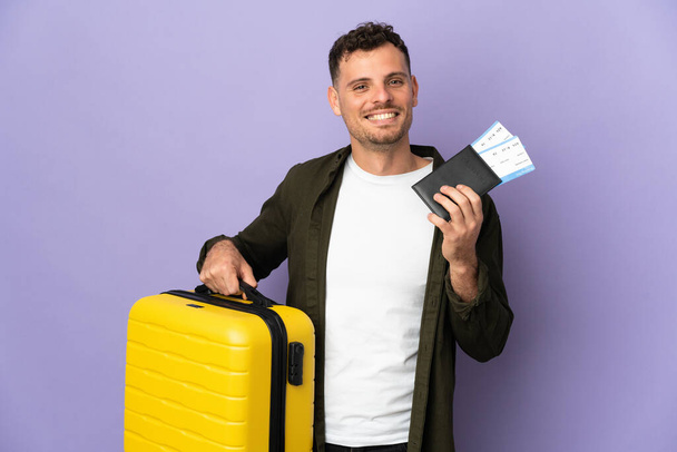 Joven caucásico guapo hombre aislado sobre fondo blanco en vacaciones con maleta y pasaporte - Foto, Imagen