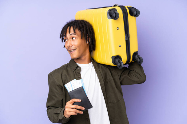 Młody, afrykański mężczyzna odizolowany na fioletowym tle na wakacjach z walizką i paszportem - Zdjęcie, obraz