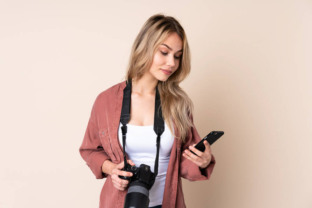 Młoda fotograf dziewczyna na odosobnionym tle trzymając kawę do zabrania i telefon - Zdjęcie, obraz