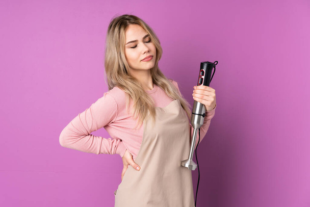 Teenager rusky dívka pomocí ruční mixér izolované na fialovém pozadí trpí bolestí zad za to, že vynaložil úsilí - Fotografie, Obrázek