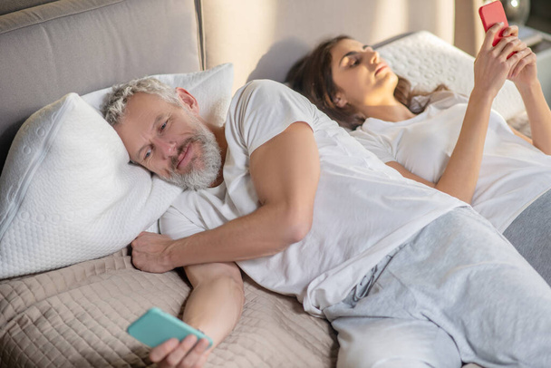 Woman and turned away man lying with smartphones - Foto, imagen