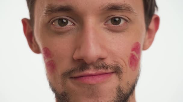Close up portrait of young ugly brunette bearded man, brown eyes, stupid smiling, show broken teeth, look at camera isolated on white background. Male with lonely grimace with red lipstick kiss marks. - Footage, Video